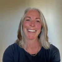 Danette Davis — Certified Orientation and Mobility Specialist Smiling woman with shoulder-length gray hair wearing a black top, standing indoors against a light background.