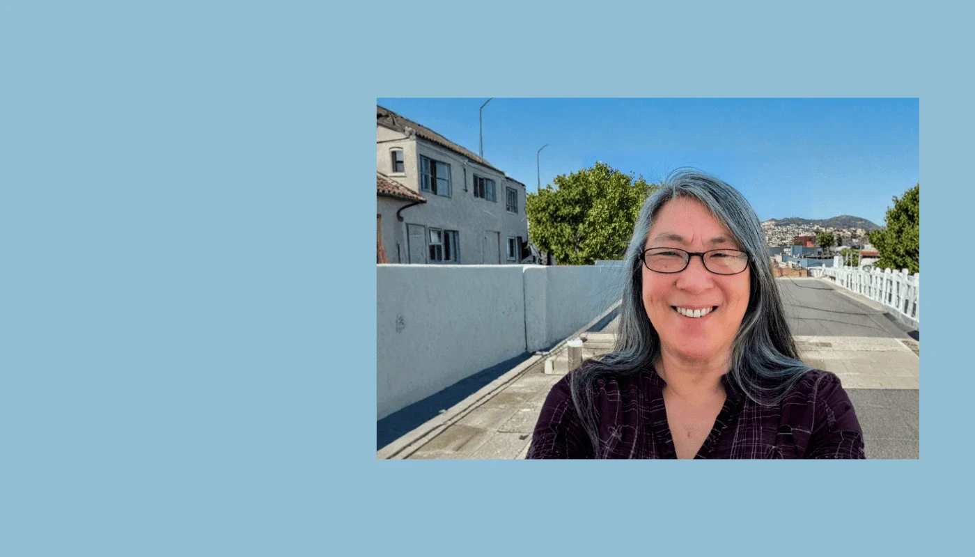 Smiling woman with long gray hair and glasses standing outdoors on a sunny day, representing the office manager of Adaptive Technology Services.