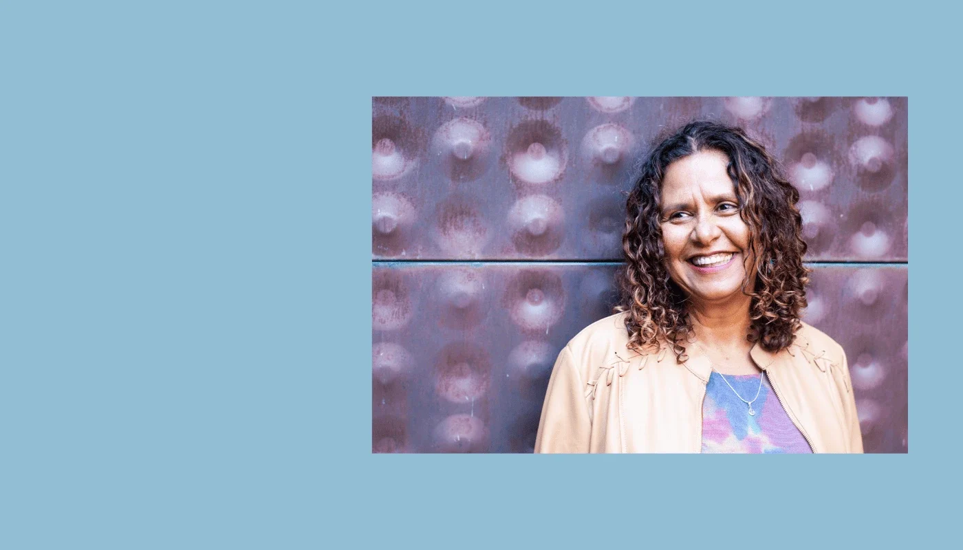 Smiling woman with curly hair standing against a textured wall, representing the co-founder of Adaptive Technology Services.