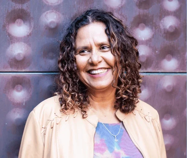 Smiling woman with curly hair standing against a textured wall, representing the co-founder of Adaptive Technology Services.